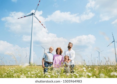 Multigeneration Family Standing On Field On Wind Farm.