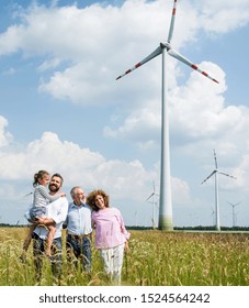 Multigeneration Family Standing On Field On Wind Farm.