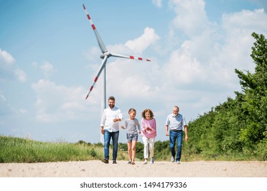 Multigeneration Family Walking On Field On Wind Farm.