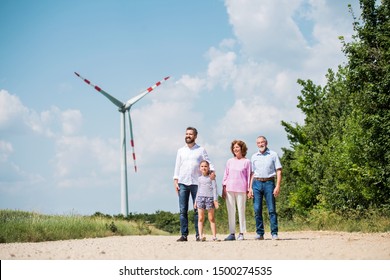 Multigeneration Family Walking On Field On Wind Farm.