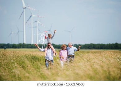 Multigeneration Family Walking On Field On Wind Farm.