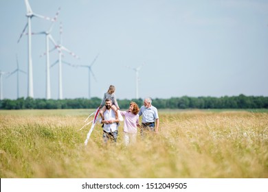 Multigeneration Family Walking On Field On Wind Farm.