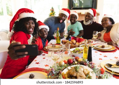 Multigeneration family wearing santa hats taking a selfie from smartphone while sitting and having lunch on dining table in the living room at home. christmas festivity tradition celebration concept - Powered by Shutterstock