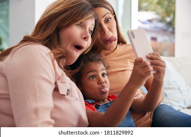 Multi-Generation Female Hispanic Family At Home Pulling Funny Faces For Selfie On Mobile Phone