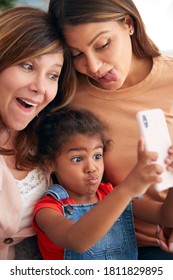 Multi-Generation Female Hispanic Family At Home Pulling Funny Faces For Selfie On Mobile Phone