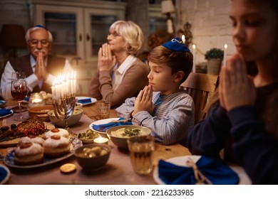 Multigeneration Jewish Family Praying During Meal At Dining Table On Hanukkah. Focus Is On Boy.