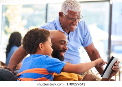 Multi-Generation Male African American Family Sitting On Sofa At Home Using Digital Tablet