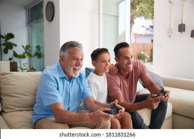 Multi-Generation Male Hispanic Family Playing Video Game At Home Sitting On Sofa Together