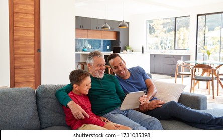 Multi-Generation Male Hispanic Family Sitting On Sofa At Home Watching Movie On Digital Tablet