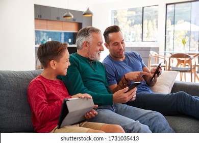 Multi-Generation Male Hispanic Family Sitting On Sofa At Home Using Mobile Phones And Digital Tablet