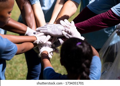 Multi-generation mixed race family spending time outside together, all wearing blue volunteer t shirts and protective gloves, collecting garbage, standing in a huddle, hand stacking, on a sunny day