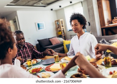 A multi-generational African-American family saying grace at dinner table and holding hands - Powered by Shutterstock