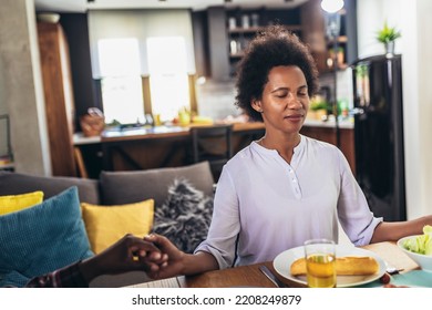 A Multi-generational African-American Family Saying Grace At Dinner Table And Holding Hands