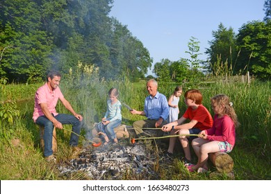 Multigenerational Family Cooking On Campfire In Field