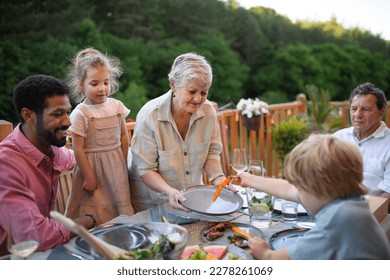 Multigenerational family eating dinner at barbecue party. - Powered by Shutterstock