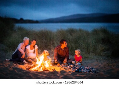 Multi-generational Family Enjoy A Beach Bonfire At Night.