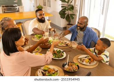 multigenerational family enjoying dinner together, raising glasses for toast at home. celebration, togetherness, happiness, dining - Powered by Shutterstock