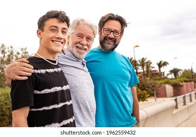 Multigenerational family group standing outdoors by the sea, hugging each other and smiling. Grandfather, son and teenage grandson. - Powered by Shutterstock