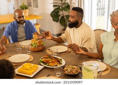 multigenerational family holding hands and praying before meal, gathered around dining table. tradition, faith, gathering, togetherness, thanksgiving, blessing - Powered by Shutterstock