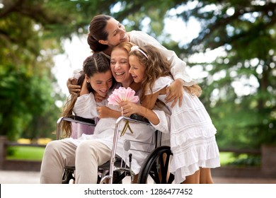 Multi-generational Family Hugging Grandmother In Wheelchair.