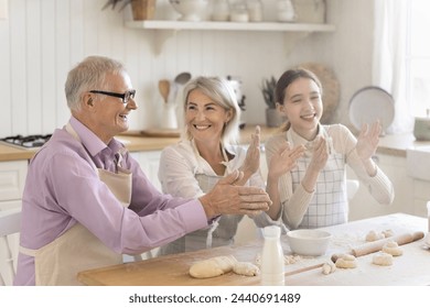 Multi-generational family laughing, having fun, joking, cooking together, clap hands, enjoy cooking process, make homemade dough for holiday pastries spend weekend time together in modern cozy kitchen - Powered by Shutterstock