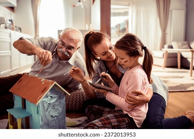 Multigenerational family painting a toy house together in the living room at home - Powered by Shutterstock