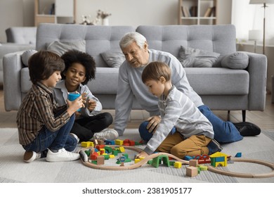 Multigenerational family play wooden railway at modern home. Senior great-grandad play railroad with three multiracial boys, siblings, cute great-grandchildren, spend pastime together in living room - Powered by Shutterstock