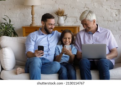 Multigenerational Family Sit On Couch Use Diverse Devices. Elderly Grandpa, His Grown Up Son, Little Grandkid Spend Time At Home Enjoy Wireless Gadgets Usage. New App, Fun, Modern Tech Overuse Concept