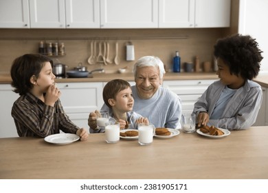 Multigenerational family, three cute great-grandchildren spend time with loving elderly great-grandpa sit in kitchen drinking milk eating delicious sweet homemade cookies, enjoy food and conversation - Powered by Shutterstock