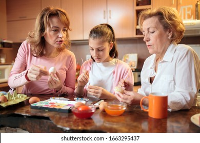 Multi-generational female Caucasian family preparing and decorating Easter eggs standing behind kitchen counter at home - Powered by Shutterstock