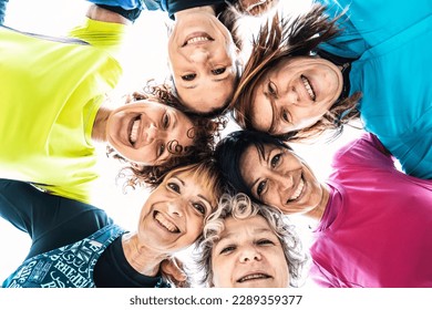 Multigenerational female friends embrace in a circle and looking down at camera after sport workout outdoor - Happy multi generational women having fun together at city park - Bright filter - Powered by Shutterstock