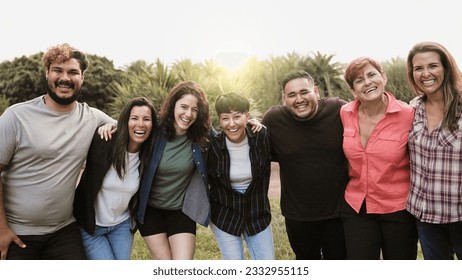 Multi-generational group of people smiling at camera outside park city during summer day - Multiracial friends celebrate holiday vacations outdoors - Powered by Shutterstock