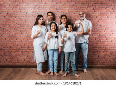 Multigenerational Indian Asian Family Showing Or Holding Glasses Full Of Milk Against Brick Wall