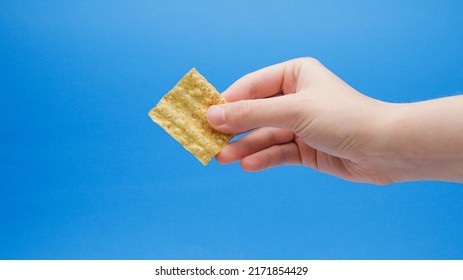 Multigrain Wheat Chip At Angle In Hand On A Blue Background