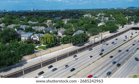 Multi-lane US 75 corridor with sound barrier wall separates expressway from upscale homes and mixed-use commercial buildings, skyline backdrop illustrating Dallas corridor-edge urban layering. USA