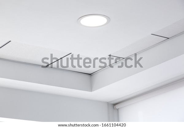 multi-level ceiling with\
three-dimensional protrusions and a suspended tiled ceiling with a\
built-in round led light in the corner of the room, close up\
details.