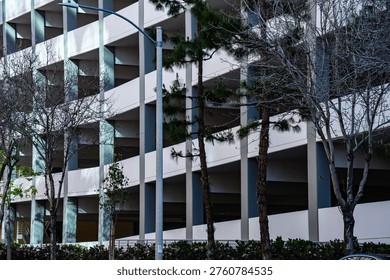 A multi-level concrete parking structure features repeating geometric patterns and is partially obscured by trees and a street light