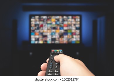 Multimedia Video Concept On TV Set In Dark Room. Man Watching TV With Remote Control In Hand.