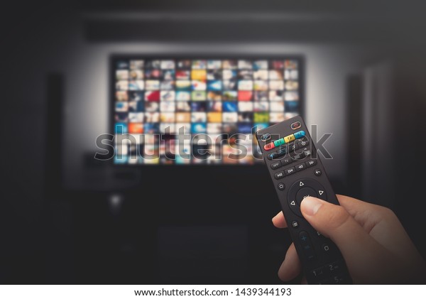 Multimedia video concept on TV set in\
dark room. Man watching TV with remote control in\
hand.