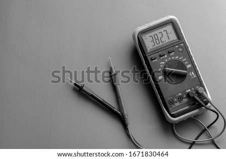 A multimeter with data on the display. Digital multimeter with probes on gray background, A multimeter is an electronic measuring instrument. View from above. Selective focus. Monochrome