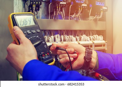 Multimeter in hands of electrician close-up against  background of electrical wires and relays. Adjustment of scheme of automation and control of electrical equipment