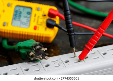 Multimeter testing damaged electrical cord for voltage, safety inspection, repair diagnosis, and fire hazard prevention.