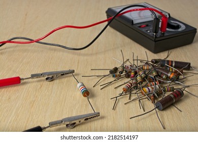 Multimeter Testing Vintage Electronic Components On Wooden Workbench. Alligator Clip Leads Are Positioned On Resistor Leads. A Pile Of Colorful Resistors Near By