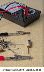 Multimeter Testing Vintage Electronic Components On Wooden Workbench. Alligator Clip Leads Are Positioned On Resistor Leads. A Pile Of Colorful Resistors Near By