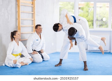 Multinational athletes in white kimonos practice Brazilian jiu Jitsu Aikido Wing chun wrestling. Training at Academy of Martial Arts martial arts hand-to-hand combat. - Powered by Shutterstock