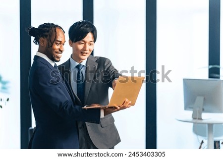 Multinational businesspeople talking while looking at laptop PC in the lobby. International business.