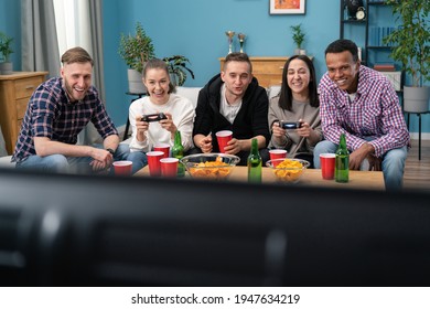 Multinational Friends Sitting At Home On Couch And Playing Video Games On Console. Cheerful Mixed Races Friends Resting In Room Sitting On Sofa. A Group Of College Students Are At A Dorm Party.