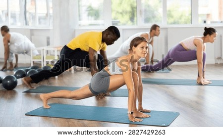 Multinational group of students practices hatha yoga greeting to sun surya namaskar during class in sports studio. Athletes perform surya namaskar