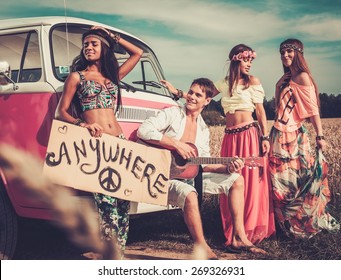 Multinational hippie hitchhikers with guitar and luggage on a road