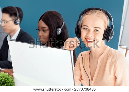 Multinational team of call centre operators speaking to customers online at modern office. Helpline consultants working in telemarketing or technical support, indoors
